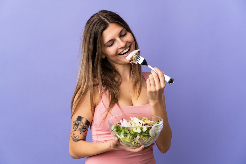 Девушка улыбается и ест салат